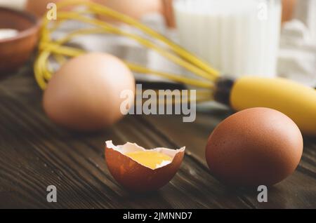 Raw organic brown chicken broken eggs with yolk flour milk and whisk on kitchen wooden table Stock Photo