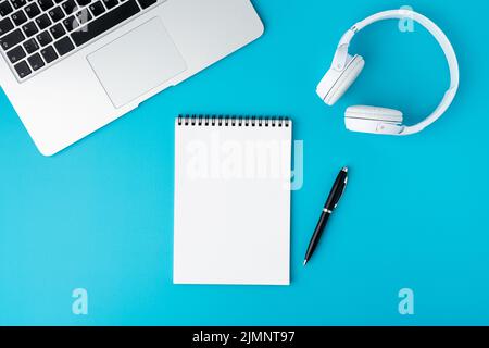 Blank spiral notepad on turquoise background with laptop, headphones and fountain pen Stock Photo