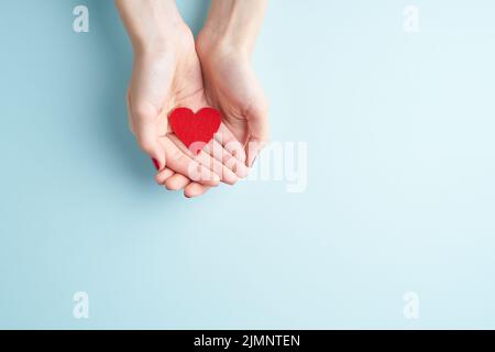 Person holding red heart in hands, donate and family insurance concept, on aquamarine background Stock Photo