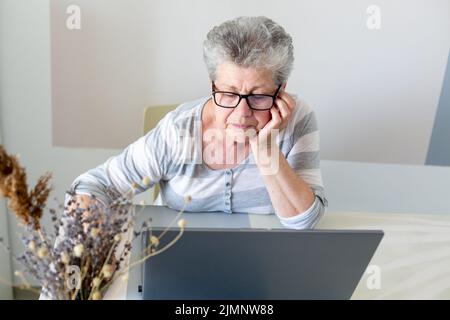Old woman working on laptop concentrated, frontal image Stock Photo