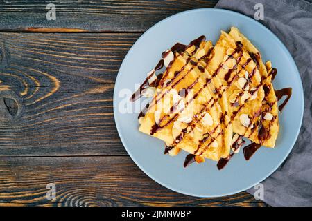 Two pancakes with chocolate syrup, almond flakes on plate, honey flows from spoon Stock Photo