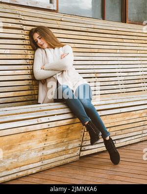 Beautiful young girl with long brown hair sits on wooden bench made of planks and rests, sleeps or dozes in fresh air. Outdoor p Stock Photo