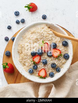 Oatmeal porridge rustic with berries, dash diet, on white wooden background top view Stock Photo