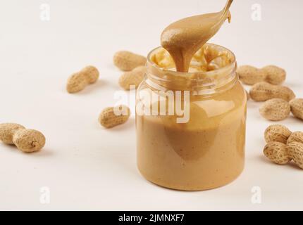 Jar of peanut butter and peanuts in shell on a white table, side view, fresh ground crushed nuts, side view Stock Photo