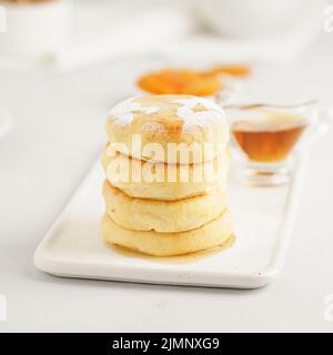 Fried cheese cakes, sweet cheese pancakes on white plate on white background. Home tea party Stock Photo