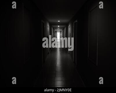 Dark mysterious corridor in building. Door room perspective in lonely quiet building with walkway heading to the light at the end of the way, black an Stock Photo