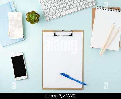 Top view of modern blue office desktop with blank notepad, computer, smartphone. Mock up, Stock Photo