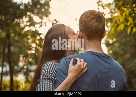 Girl kissing boy in cheek in the park, concept of teen love Stock Photo