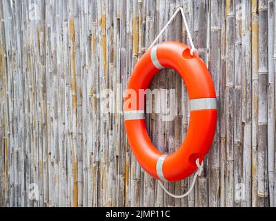 An orange lifebuoy, safety ring hanging on bamboo fence wall background with copy space. Rescue equipment. Lifesaver, Safety concepts. Stock Photo