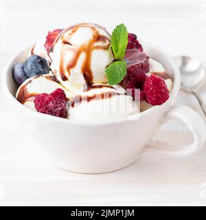 Balls of vanilla ice cream in mug with raspberry and blueberries, chocolate Stock Photo