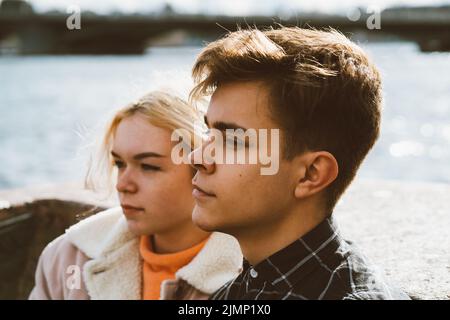 Teenagers in love sit on the waterfront in the city center, resting in autumn sun. Concept the first teenage love, the beginning Stock Photo