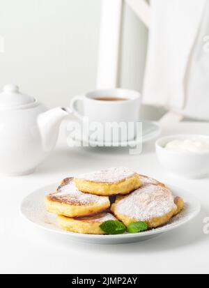 Fried cheese cakes, sweet cheese pancakes on white plate on white background. Home tea party Stock Photo