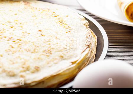 Stack of French crepes in frying pan on wooden kitchen table Stock Photo