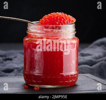 Fresh grainy red caviar in a glass jar on a wooden table Stock Photo