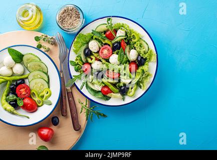 Preparation of Green Salad with mozzarella cheese, black olives, arugula and tomato on blue table background Stock Photo