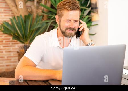 Young caucasian man working using laptop while talking on telephone at the terrace. Stock Photo