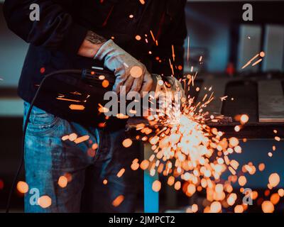 Heavy Industry Engineering Factory Interior with Industrial Worker Using Angle Grinder and Cutting a Metal Tube. Contractor in S Stock Photo