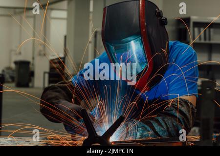Professional Heavy Industry Welder Working Inside factory, Wears Helmet and Starts Welding. Selective Focus Stock Photo