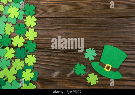 Happy Saint Patrick's mockup of handmade felt hat and shamrock clover leaves on wooden background. Stock Photo