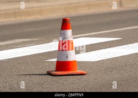 Traffic cone with orange and white stripes standing on street Stock Photo