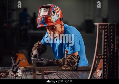 Professional Heavy Industry Welder Working Inside factory, Wears Helmet and Starts Welding. Selective Focus Stock Photo