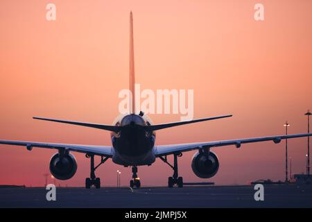 Rear view of airplane taxiing to runway for take off. Traffic at airport at dawn. Stock Photo