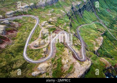 Aerial view of a winding dirt road cutting through a lush green forest ...