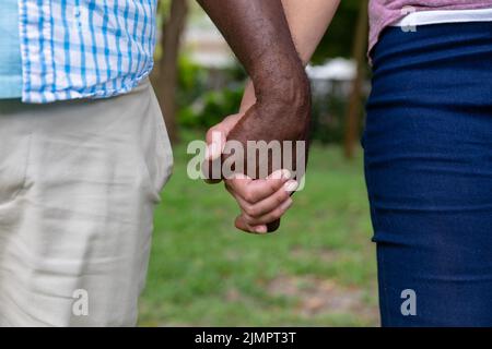 Midsection of multiracial senior couple holding hands in backyard Stock Photo