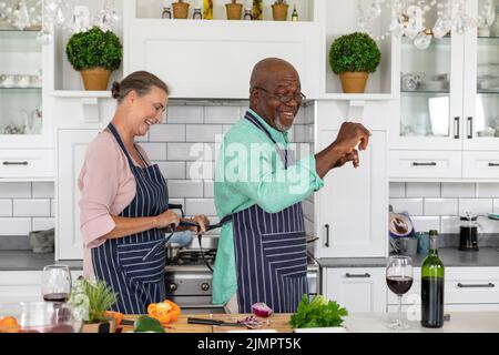 Happy multiracial senior couple dancing in kitchen while cooking food together at home Stock Photo