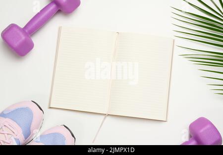 Open blank notebook, a pair of sports gym shoes and dumbbells on a white background. Place for recording, top view Stock Photo