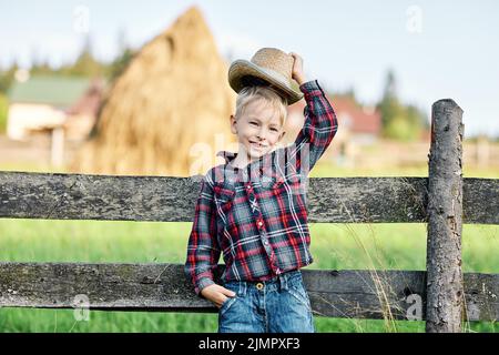 Close up portrait of little boy in hat leaned on wooden fence Stock Photo