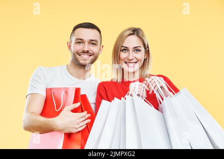 Young happy couple holding shopping bags in hands over yellow background Stock Photo