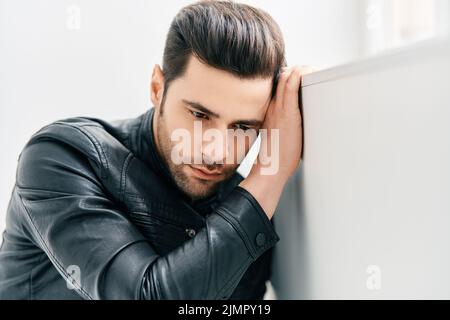 Portrait of handsome thoughtful man sitting on floor leaning to the wall Stock Photo