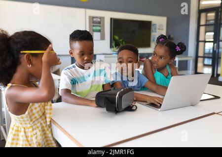 African american elementary school students using vr glasses and laptop at desk in classroom Stock Photo
