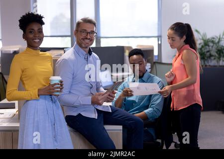 Portrait of happy biracial colleagues by advisors discussing over document at modern workplace Stock Photo