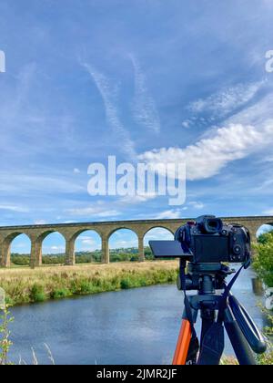 A full frame mirrorless digital camera on a tripod filming or shooting photographs whilst aimed at a beautiful landscape scene - Arthington Viaduct. Stock Photo