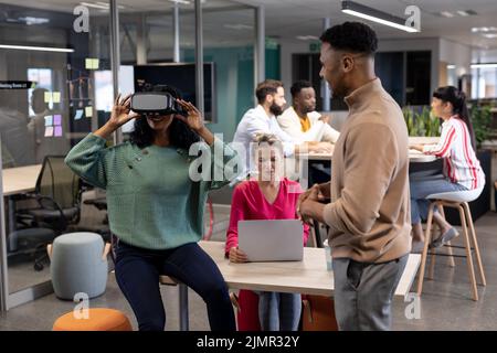 Hispanic businesswoman discussing with african american businesswoman wearing vr headset in meeting Stock Photo
