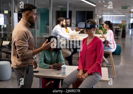Hispanic businesswoman discussing with caucasian businesswoman wearing vr simulator in meeting Stock Photo