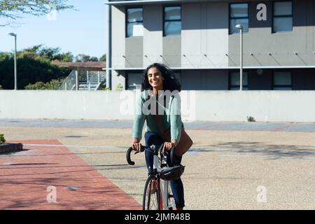 Happy young biracial businesswoman commuting through bicycle in city on sunny day Stock Photo