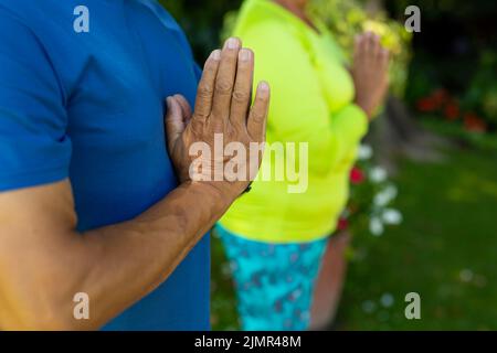 Midsection of biracial senior husband with senior wife practicing prayer position in yard Stock Photo