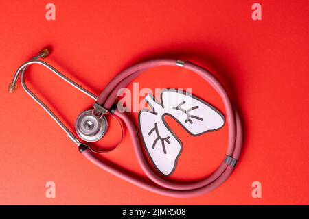 Overhead view of white paper lungs with pink stethoscope against red background, copy space Stock Photo