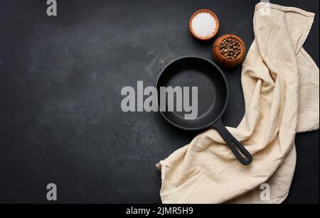 Empty black round cast iron frying pan with handle on black table, top view. Copy space Stock Photo