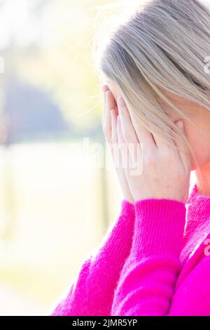 Sad tired young beautiful blonde woman with her face in her hands being frightened, having anxiety or headache migraine or depre Stock Photo