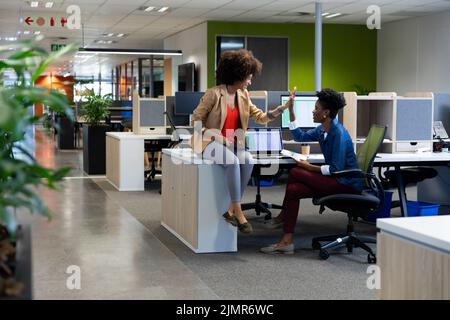 Happy biracial businesswomen giving high-five in meeting while sitting in cubicle at workplace Stock Photo