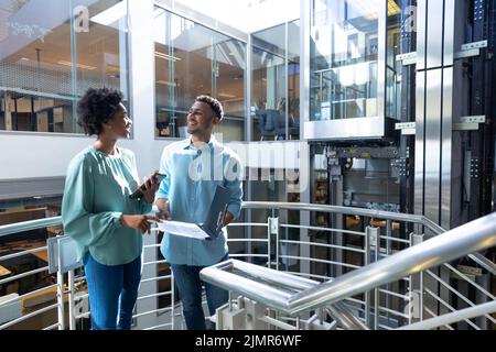 Happy african american professionals discussing over file at staircase in workplace Stock Photo