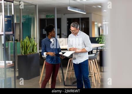Biracial male and female professionals discussing over file while standing together at workplace Stock Photo