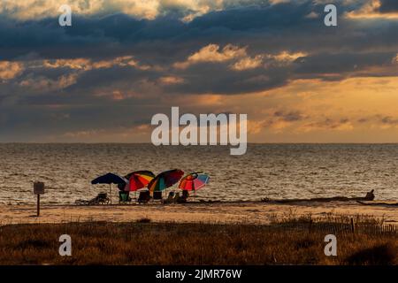 Colorful beach umbrellas are set up on a Dauphin Island, Alabama, beach under a dramatic sky in a composite image. Stock Photo