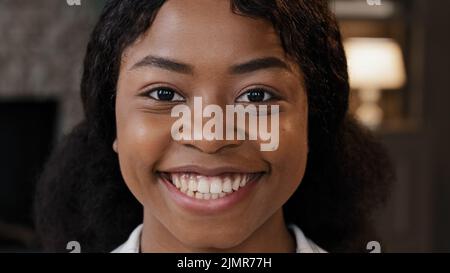 Extreme close up female face with perfect skin healthy millennial african woman looking at camera indoors happy 20s 30s girl with white toothy smile Stock Photo