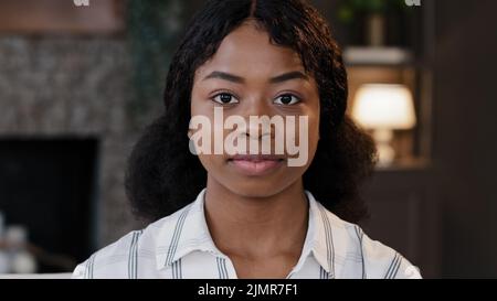 Close up female portrait indoors african 20s student girl 30s millennial woman wife girlfriend mother looking at camera standing at home office. Calm Stock Photo