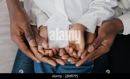 Close-up female male and child hands of african family holding cardboard shape of house picture of home dream of housing relocation renting new flat Stock Photo